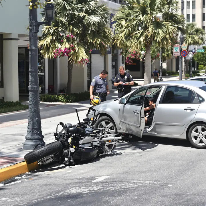 Motorcycle on its side near a sedan with a dented door as an officer takes notes