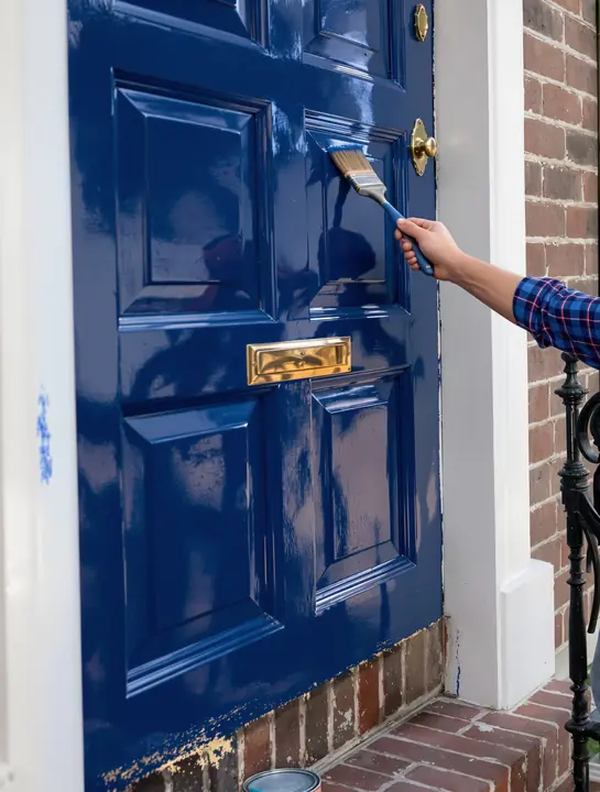 Brushing gloss paint onto a paneled front door on a brick stoop