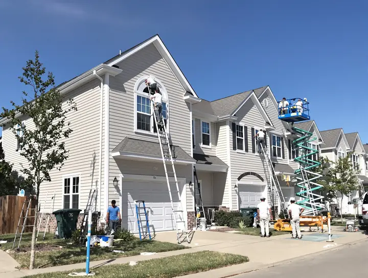 Painters on ladders repainting townhome siding and trim in an HOA community
