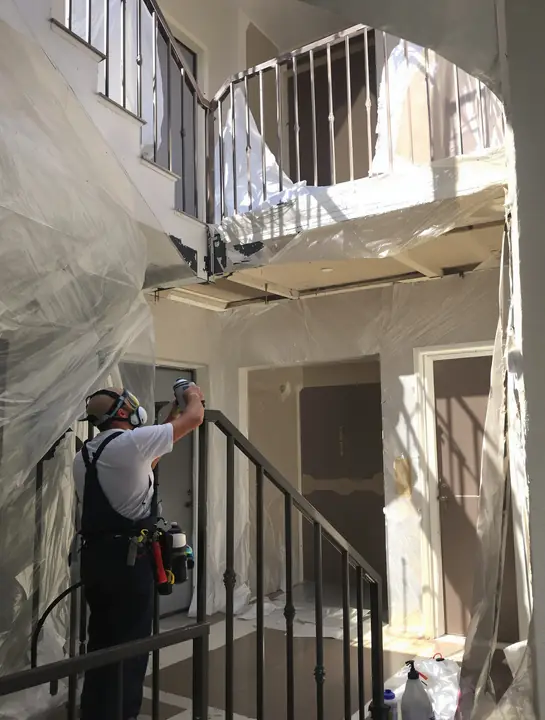Painter spraying bronze paint on apartment stair railings and metal doors
