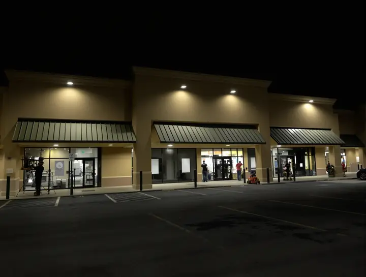Night crew under work lights repainting a strip center facade