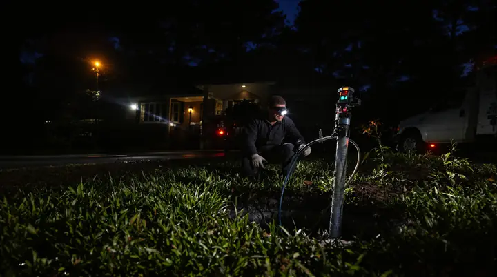 Plumber with a headlamp running a sewer camera into a front yard cleanout at night in Charlotte