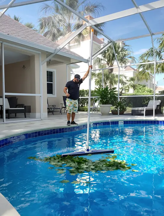 Tech skimming leaves out of a pool under a screened lanai