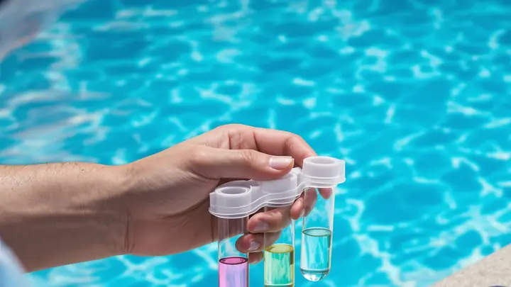 Water test vials held over a blue pool