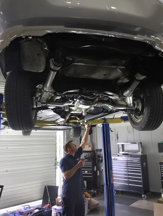 Inspector checking the exhaust and suspension of a car on a lift