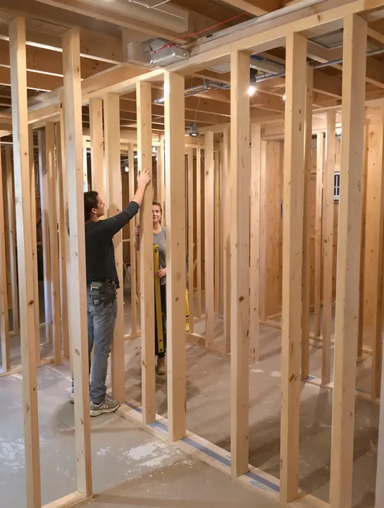 A homeowner holding a level while a carpenter frames her basement