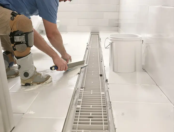 Tile setter laying large porcelain tile on a sloped shower floor