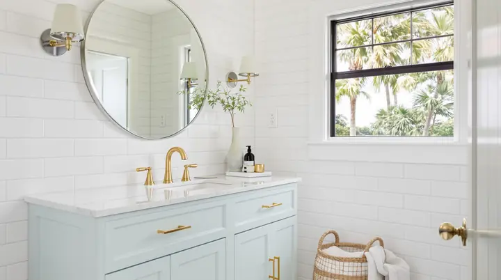 Finished guest bath with a spa blue vanity, brass faucet and a round mirror