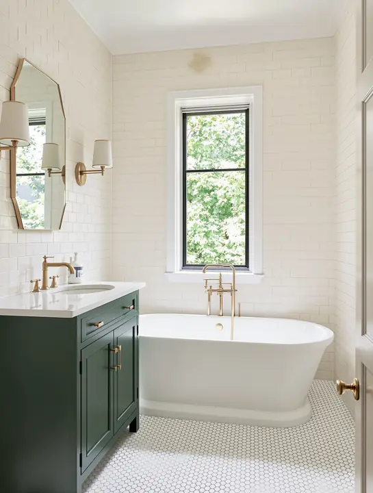 Primary bath with cream handmade tile, a green vanity and a white tub under a tall window