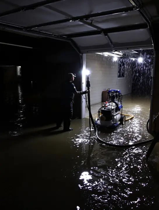 Worker in waders setting a pump in a flooded garage at night