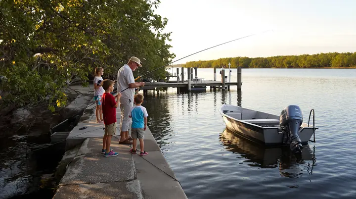 A grandfather teaching two grandkids to fish off a seawall on a canal