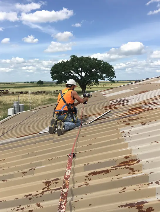 Roofer fastening panels on a rusting metal building roof in Central Texas