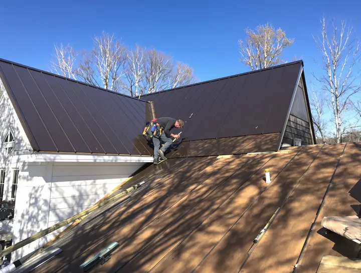 Roofer seaming dark bronze standing seam metal panels on a farmhouse outside Minneapolis