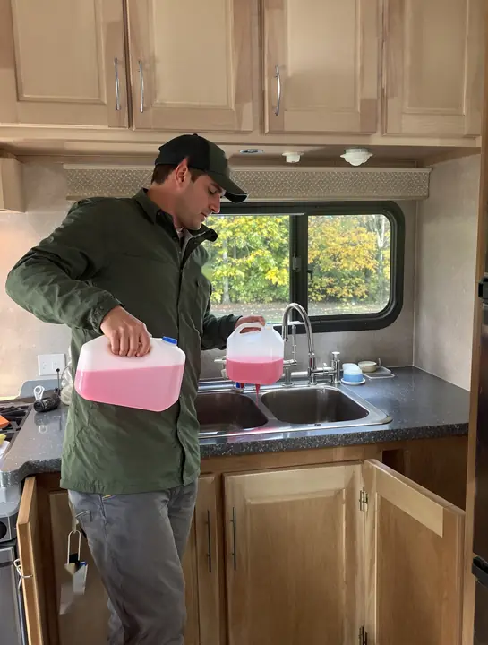Tech pouring pink RV antifreeze into a travel trailer sink drain