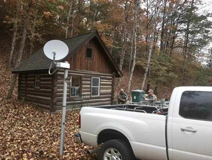 A small dish on a pole beside a hunting camp in the woods
