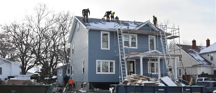 Snowbelt crew on pump jacks hanging new blue siding on a Buffalo double house in early December