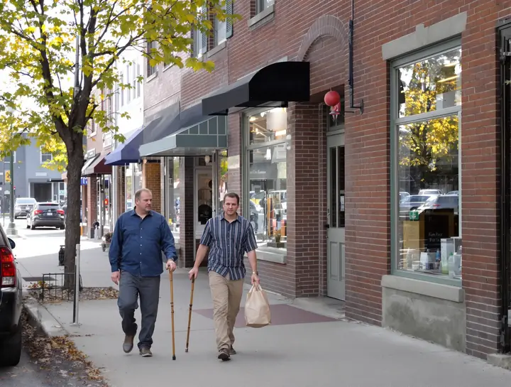 A client with a cane walking with his son on a small town main street