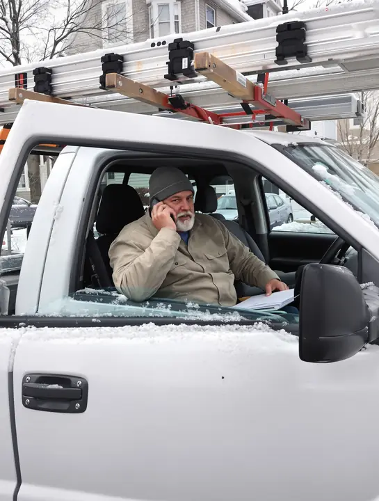 A roofer on the phone in his truck cab with a folder of papers on his lap
