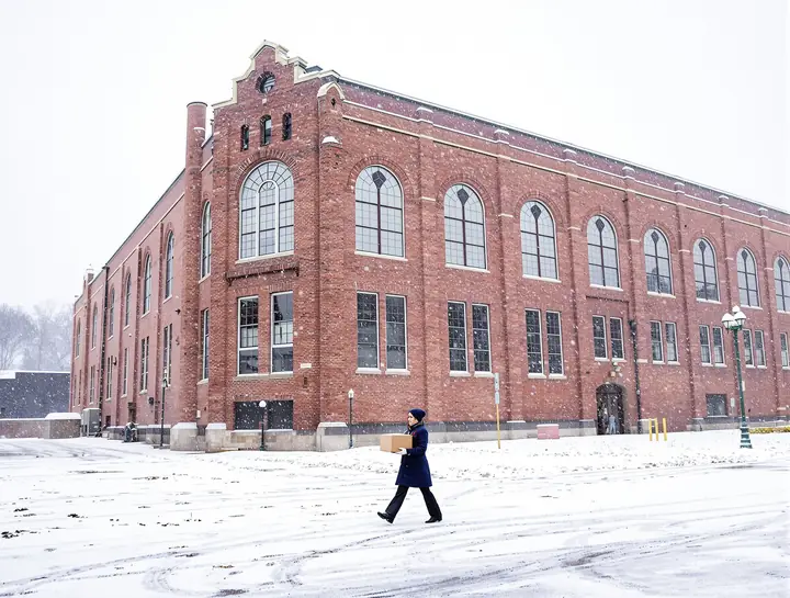 Maureen carrying a box of files across a snowy lot to the mill building