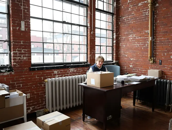 Maureen opening a shoebox of receipts at her desk in an old brick mill office