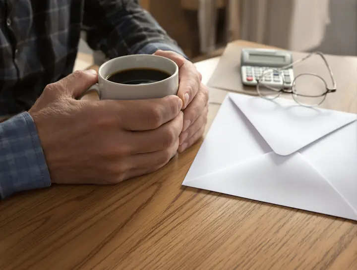 An owner with coffee, a calculator and an envelope at the kitchen table