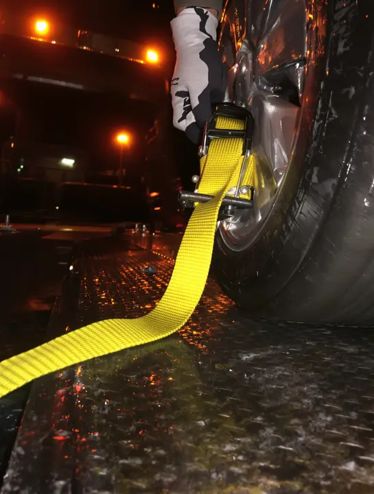 Driver ratcheting a wheel strap over a tire on the flatbed deck