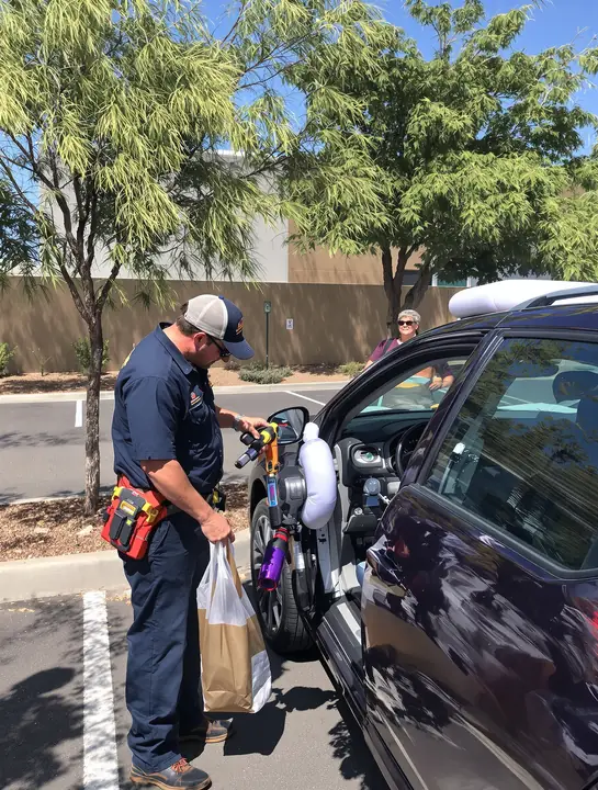 Tech opening a locked car door with an air wedge in a sunny parking lot