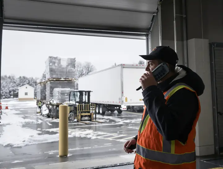 Warehouse lead taking a call on a rugged handset at the dock door