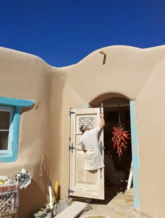 Carved wood entry door being hung in a deep adobe opening off Canyon Road
